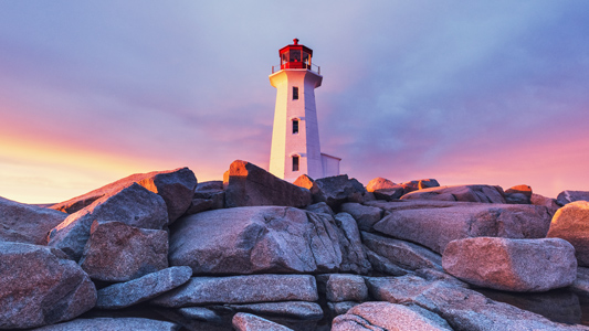 A lighthouse surrounded by boulders with a colourful sky around.