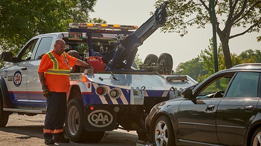 Image showing white CAA tow truck with operator wearing flourescent orange vest hooking up a sedan for a tow.