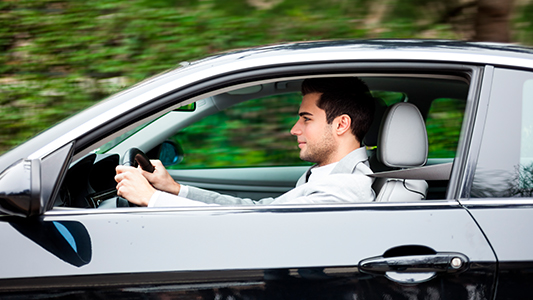 A man driving in a black two-door car.