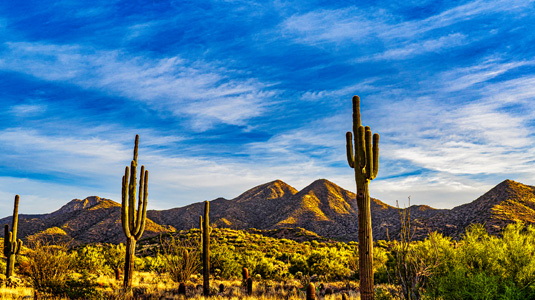 Blue sky with clouds above a sunlit desert landscape.