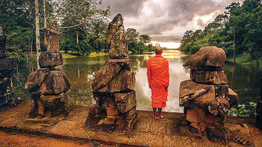 Monk looking over water in ancient landscape.