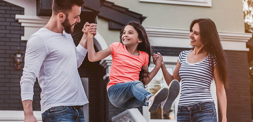 Mother and Father swinging their child happily outside of their home